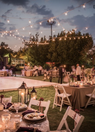 Outdoor event with stage, tables and chairs, and lights strung across space. 