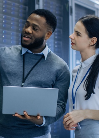 IT Technician with a Laptop Computer points out the server racks to a coworker. 