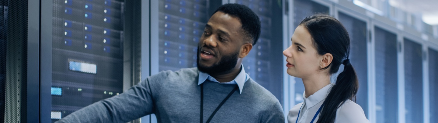 IT Technician with a Laptop Computer points out the server racks to a coworker.  