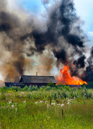 A farm on fire with black smoke next to haybales 