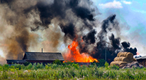 A farm on fire with black smoke next to haybales 