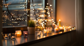 Tea light candles in holders with Christmas lights hanging in a window.