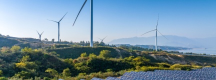 Solar panels and wind turbines on a hill with a view of mountains in the distance.  