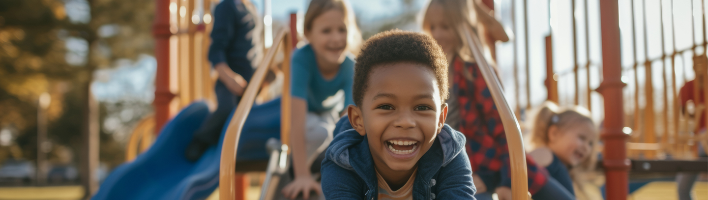 A boy smiles while on the playground with other children behind him