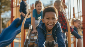 A boy smiles while on the playground with other children behind him