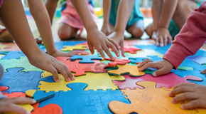 Children sit on a puzzle mat with their hands reaching for large, colorful puzzle pieces. 